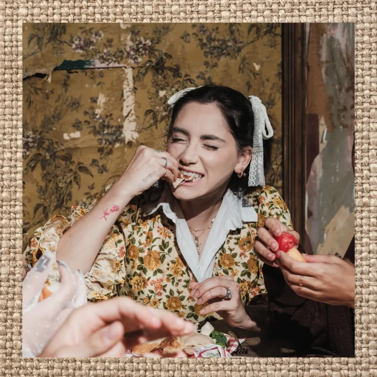 Woman enjoying food at a table, surrounded by hands sharing a meal, in a textured editorial frame.